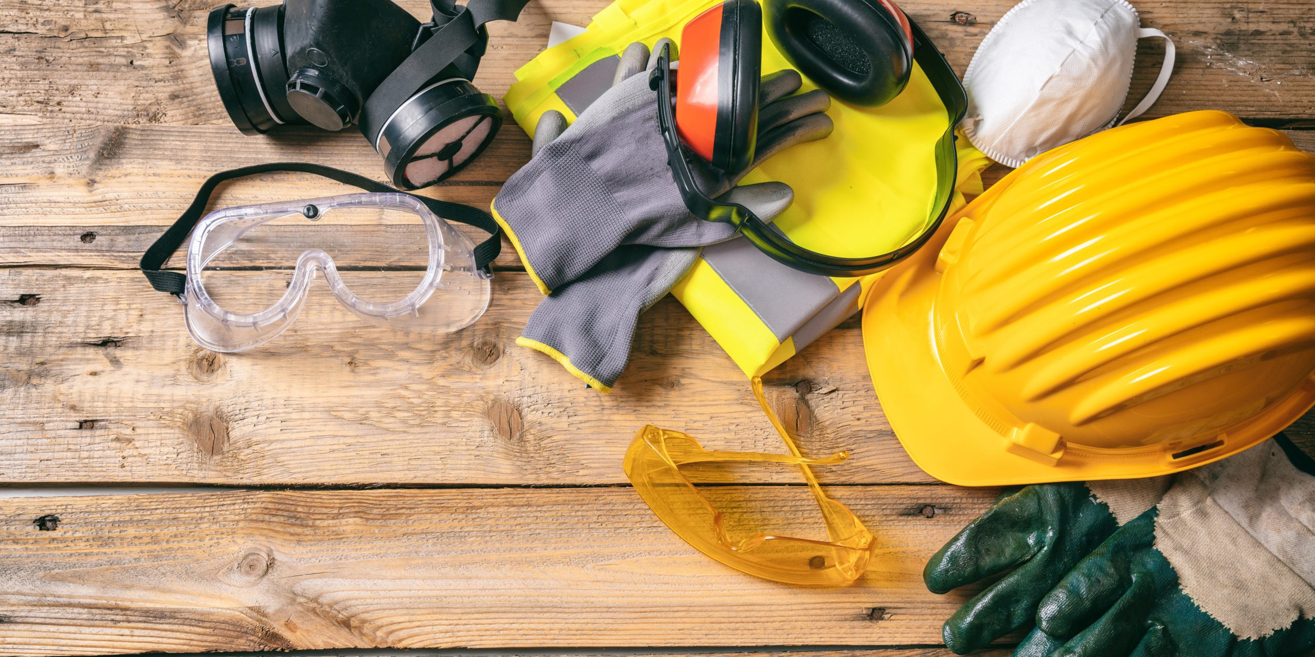 Construction safety. Protective hard hat, headphones, gloves and glasses on wooden background, copy space, top view